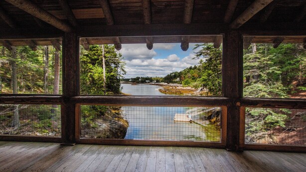 A wooden cabin with large windows overlooking a forested area and a river. - 3 charming cottages sleeping 14 on an ocean cove, 21-acre forest property (Phippsburg)