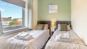 A hotel room with two beds, a window, a painting on the wall, and a nightstand with a lamp.