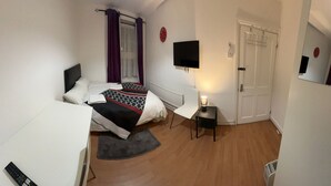 Una camera da letto con un letto, una sedia, un televisore e una porta.