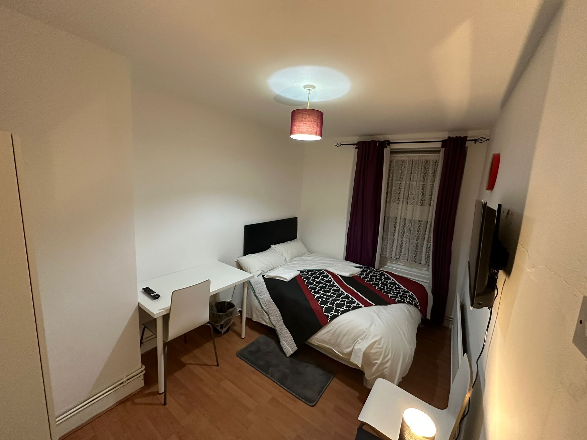 A small, neatly arranged bedroom with a bed, desk, chair, and a ceiling light.