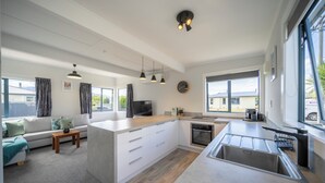 Eine moderne Küche mit einer zentralen Kochinsel, einem Essbereich mit Sofa und Couchtisch sowie großen Fenstern mit Blick nach draußen.