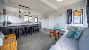 Eine moderne Küche mit einer zentralen Kochinsel, Barhocker, Pendelleuchten und einer gemütlichen Wohnbereitschaft mit Sofa und Kissen.