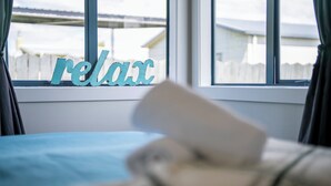 Ein Schlafzimmer mit einem Bett, einem Fenster mit einem Schild mit der Aufschrift 'relax' und Blick auf einen weißen Zaun.