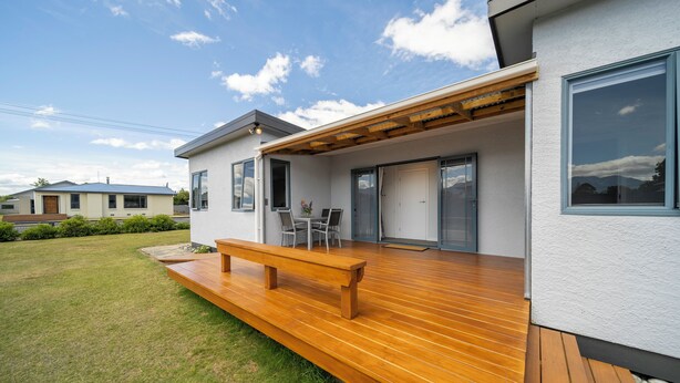 Ein modernes Haus mit einer Holzterrasse, einer Terrasse mit einer Bank und einem wolkenlosen Himmel.