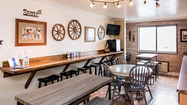 A restaurant with wooden tables and chairs, a bar area, and a television mounted on the wall. - Western Inn (Tremonton)