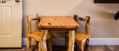 A wooden dining table with four chairs, a white door with a lock, and a wooden shelf with items on it.
