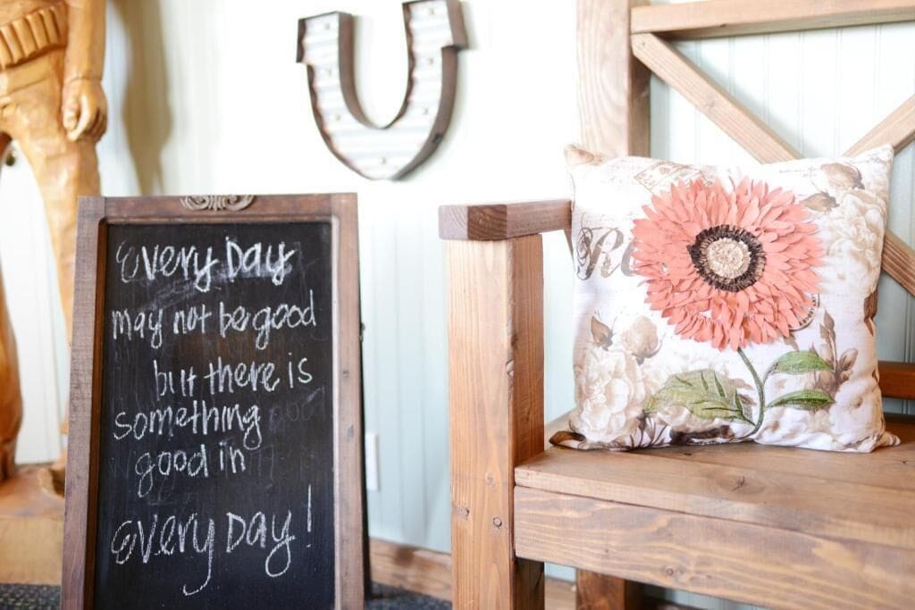 A wooden chair with a floral pillow and a chalkboard with a motivational quote.