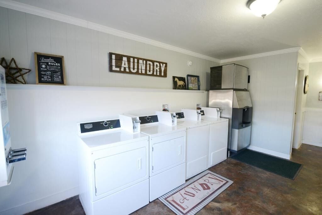 Un área de lavandería con un letrero en la pared que dice "LAUNDRY", un refrigerador de acero inoxidable y un juego de lavadoras blancas.