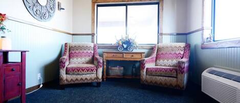 A room with two patterned armchairs, a wooden desk with a vase of flowers, a large mirror, and a radiator.