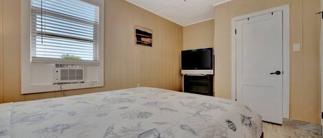 Ein Schlafzimmer mit Bett, Deckenventilator, Fernseher, Tür und Fenster mit Jalousien.