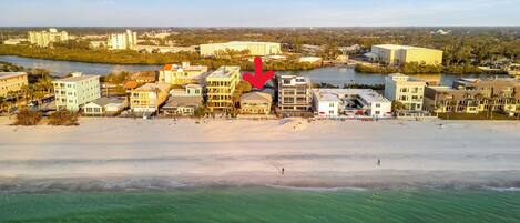 An aerial view of a coastal hotel area with buildings along the beachfront, a clear view of the ocean, and a river in the background.