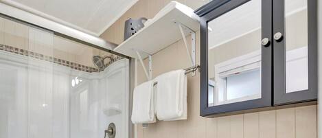 Un baño moderno con ducha envuelta en vidrio, inodoro blanco, tocador con espejo y lavabo.