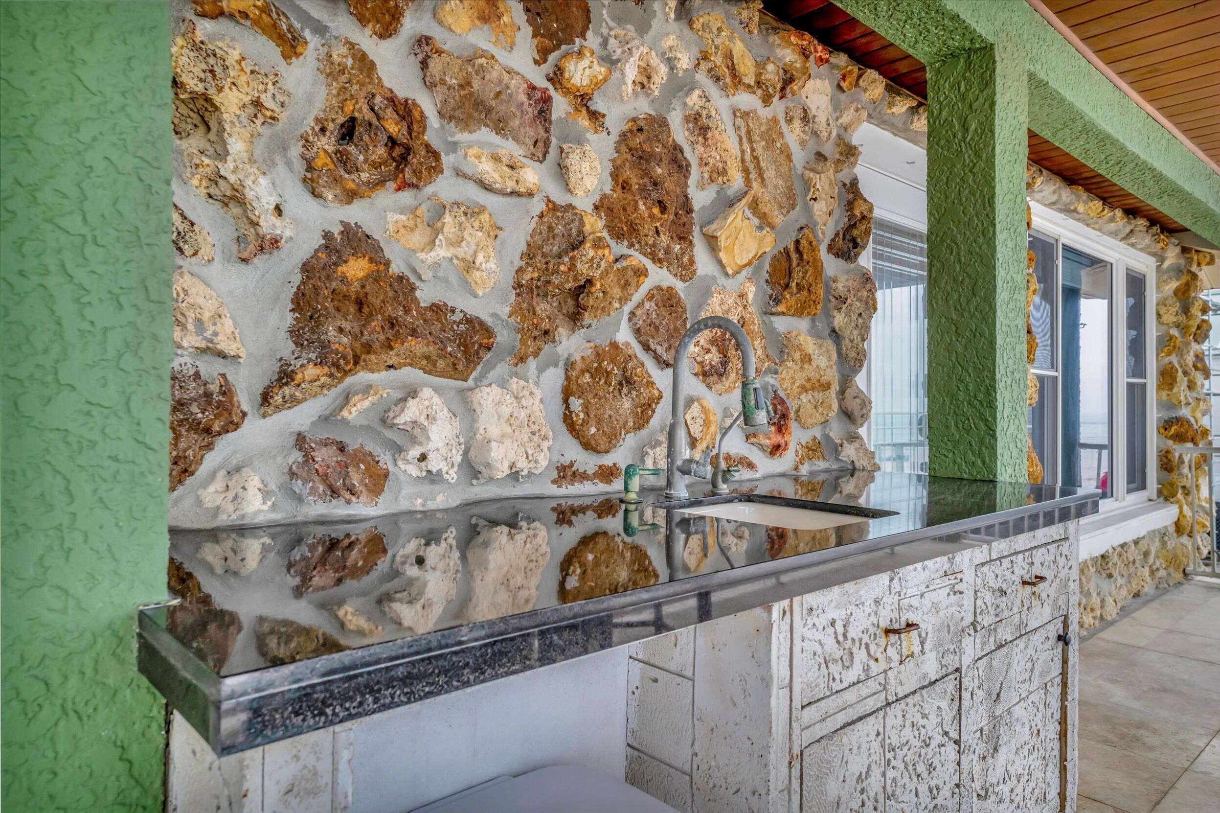 Una cocina con salpicadero de pared de piedra, un lavamanos de acero inoxidable y una pared de acento verde.