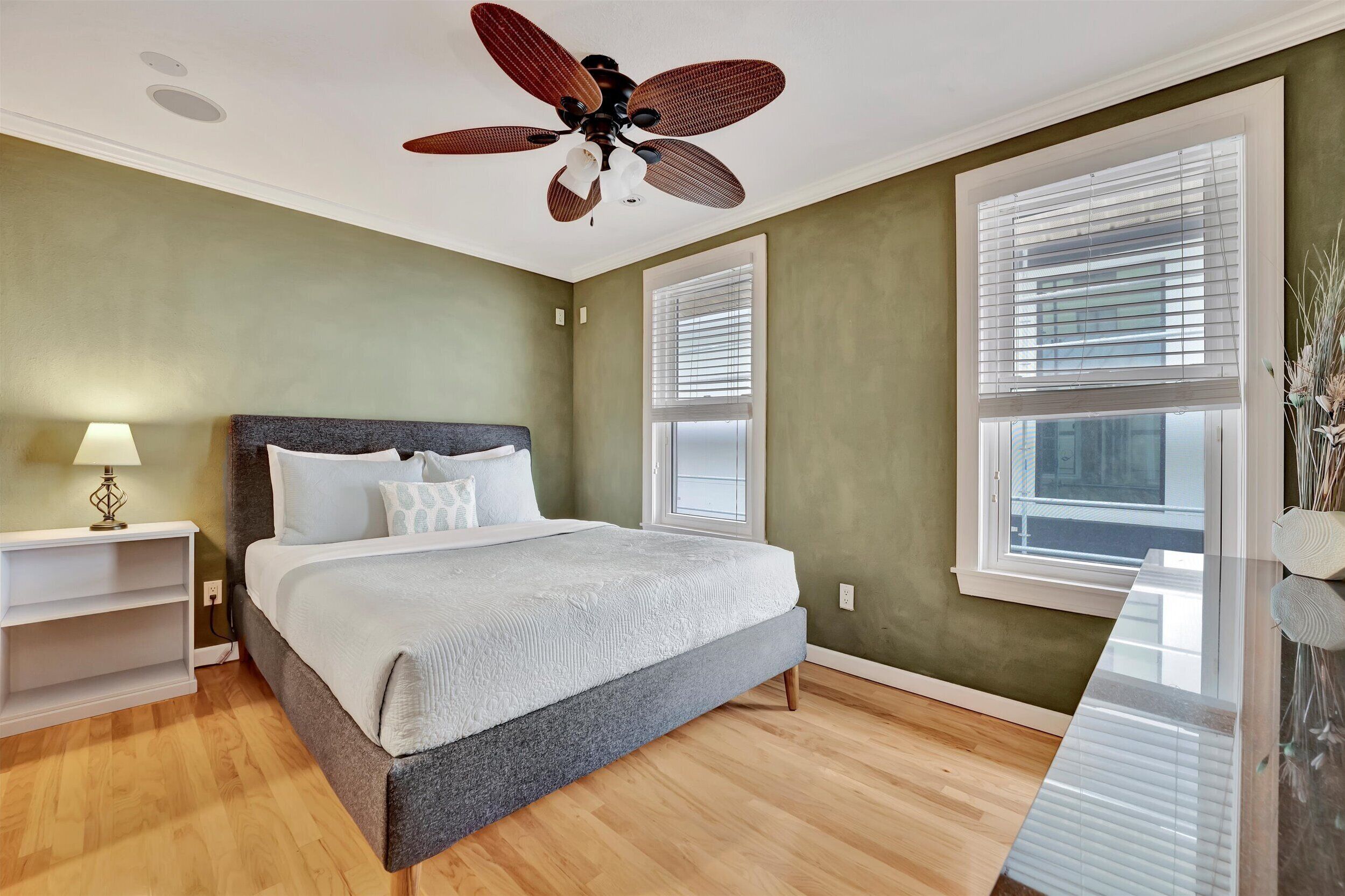 A bedroom with a bed, a ceiling fan, a nightstand, and a window with blinds.