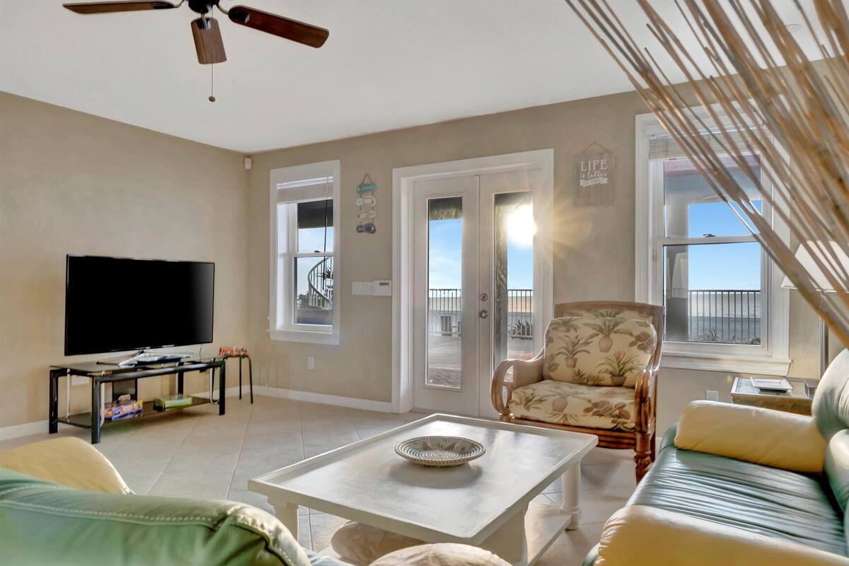 Una sala de estar con televisión, mesa de centro, sofá, sillón y puerta al balcón.