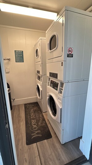 Une buanderie équipée d’une machine à laver et d’un sèche-linge superposés, d’un panneau indiquant qu’il est interdit de fumer et d’un autre panneau détaillant les règles d’utilisation de la buanderie.