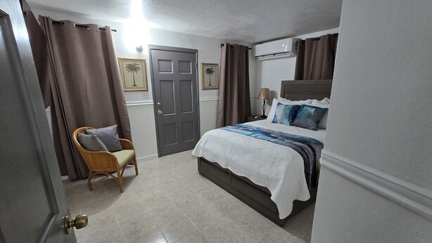 A bedroom with a bed, a chair, a door, and an air conditioning unit. - Charming 2- Bedroom Apartment with AC, WiFi in St Thomas' East End (St Thomas)