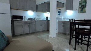 A compact kitchen with grey cabinets, a dining area with a wooden table and chairs, and a beige sofa. - Charming 2- Bedroom Apartment with AC, WiFi in St Thomas' East End (St Thomas)