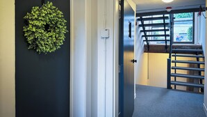 A hallway with a black door, a green wall-mounted decoration, a white wall switch, and a window with a view of the outside.