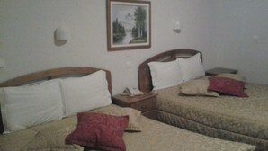 A hotel room with two beds, each with a wooden headboard, white and beige bedding, and red and beige pillows. There is a framed picture on the wall above the beds. - Residencial Pinto  (Guarda)