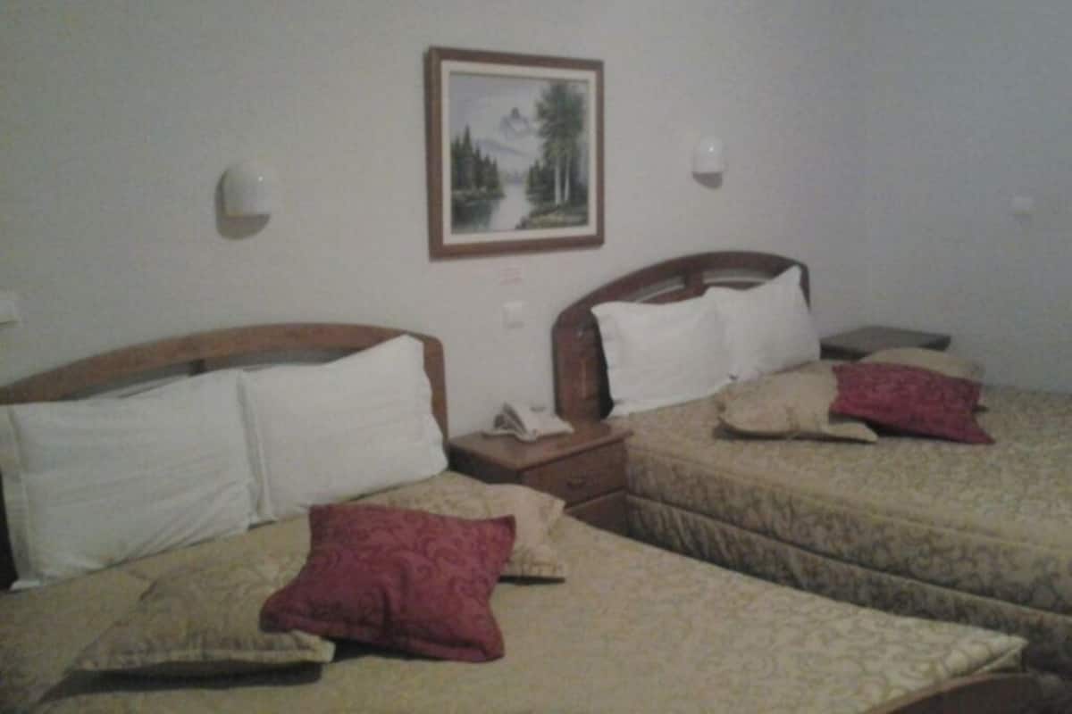 A hotel room with two beds, each with a wooden headboard, white and beige bedding, and red and beige pillows. There is a framed picture on the wall above the beds.