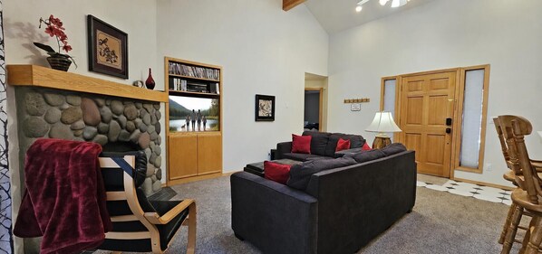 A living room with a stone fireplace, a sofa, a chair, and a bookshelf. - Whistler 19 (Bend)