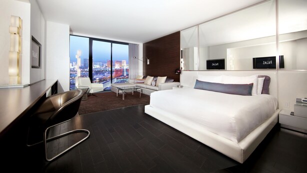Una habitación de hotel moderna con una cama grande, un escritorio, una silla y un sofá. Hay un ventanal con vistas a la ciudad.
