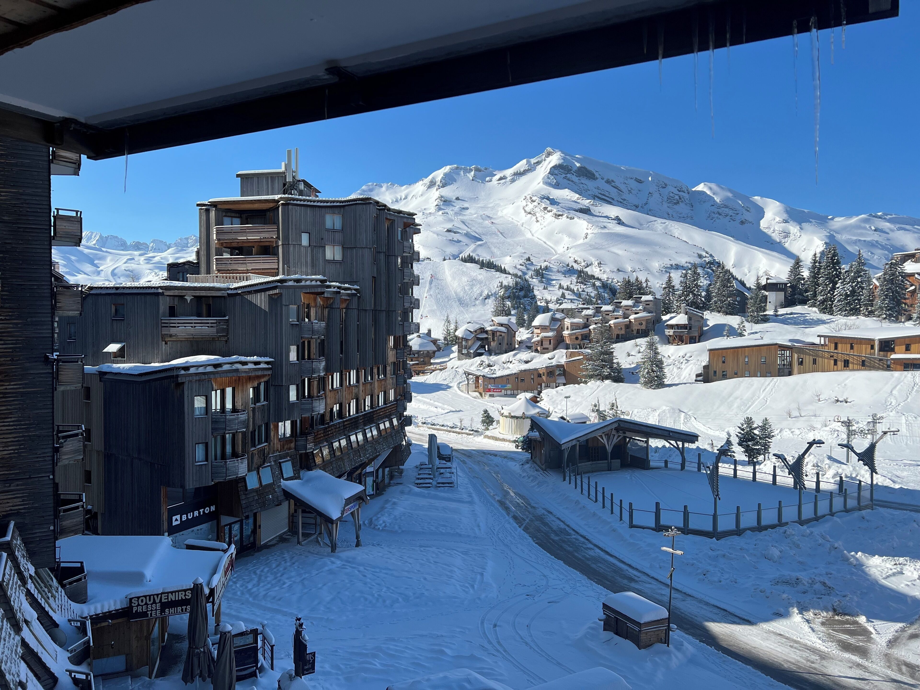 A snow-covered town with a mix of modern and traditional buildings, including a prominent multi-story structure with balconies.