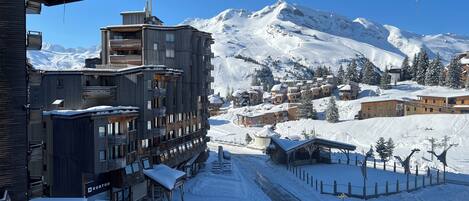 A snow-covered town with a mix of modern and traditional buildings, including a prominent multi-story structure with balconies.