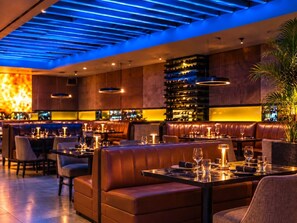 A restaurant with leather booths, tables set with wine glasses, and a bar area with shelves of bottles. - Beachfront Luxury Condo Pool   Walk 2 eat (Carolina)