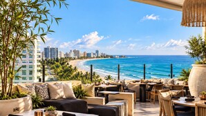 An outdoor seating area with tables and chairs, overlooking a beach and ocean. - Beachfront Luxury Condo Pool   Walk 2 eat (Carolina)