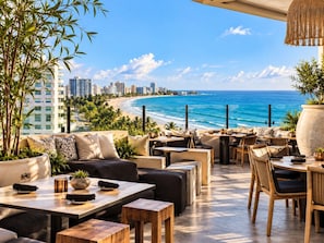 An outdoor seating area with tables and chairs, overlooking a beach and ocean. - Beachfront Luxury Condo Pool   Walk 2 eat (Carolina)