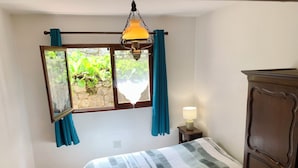 Une chambre à coucher avec un lit, une table de chevet avec une lampe, une commode en bois et une fenêtre avec des rideaux.