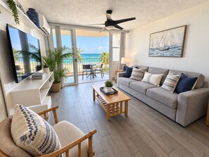 Sala de estar con sofá, una mesa de centro y televisor. Tiene un balcón con vista a la playa.