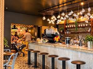 Una zona de bar con taburetes, una máquina de café y tazas colgando.