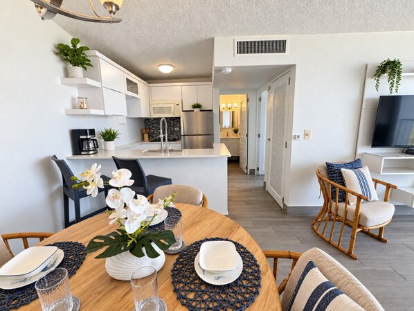 Cocina moderna con armarios blancos, refrigerador de acero inoxidable y comedor con una mesa redonda dispuesta para cuatro.