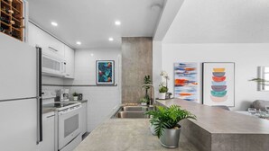 Una cucina moderna con mobili bianchi, un lavello in acciaio inossidabile e un piano di lavoro in cemento. Sul piano ci sono due piante in vaso.