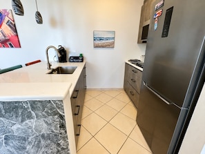 A kitchen with a marble countertop, a stainless steel refrigerator, and a tiled floor.