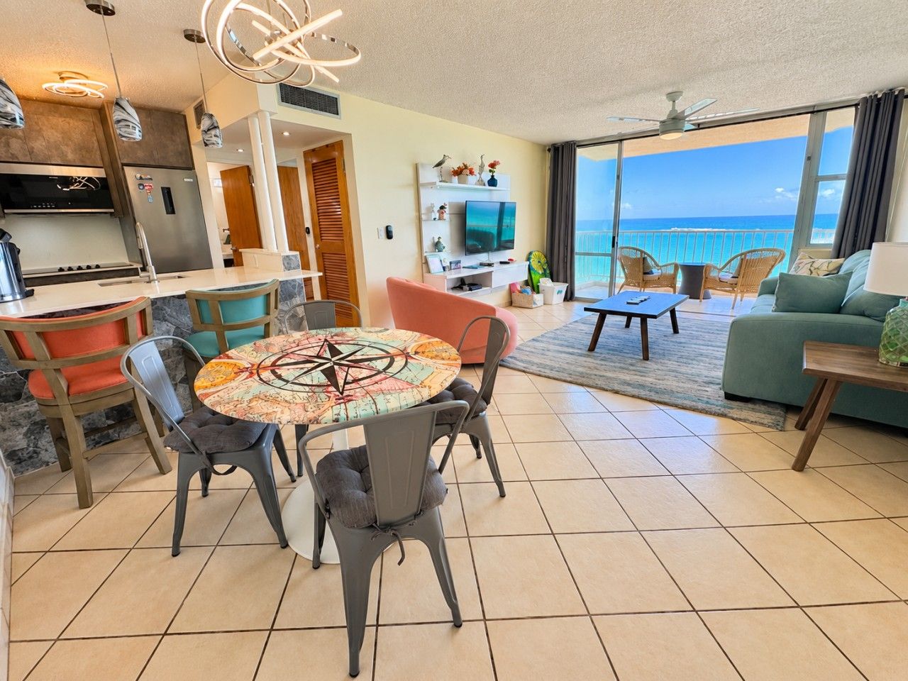 A modern living room with a dining area, kitchen, and a balcony with a view of the ocean.