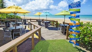 Ein Restaurant direkt am Strand mit Außenplätzen, einer Holzterrasse und einem Wegweiser mit Pfeilen.