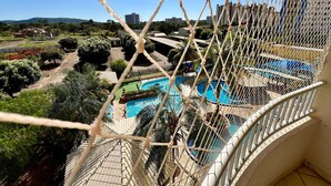 Vista de uma varanda com vista para uma piscina, cercada por vegetação e edifícios.