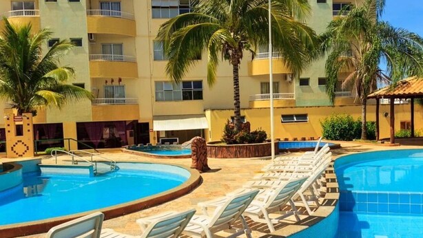 Área de piscina de hotel com várias piscinas, espreguiçadeiras e palmeiras.