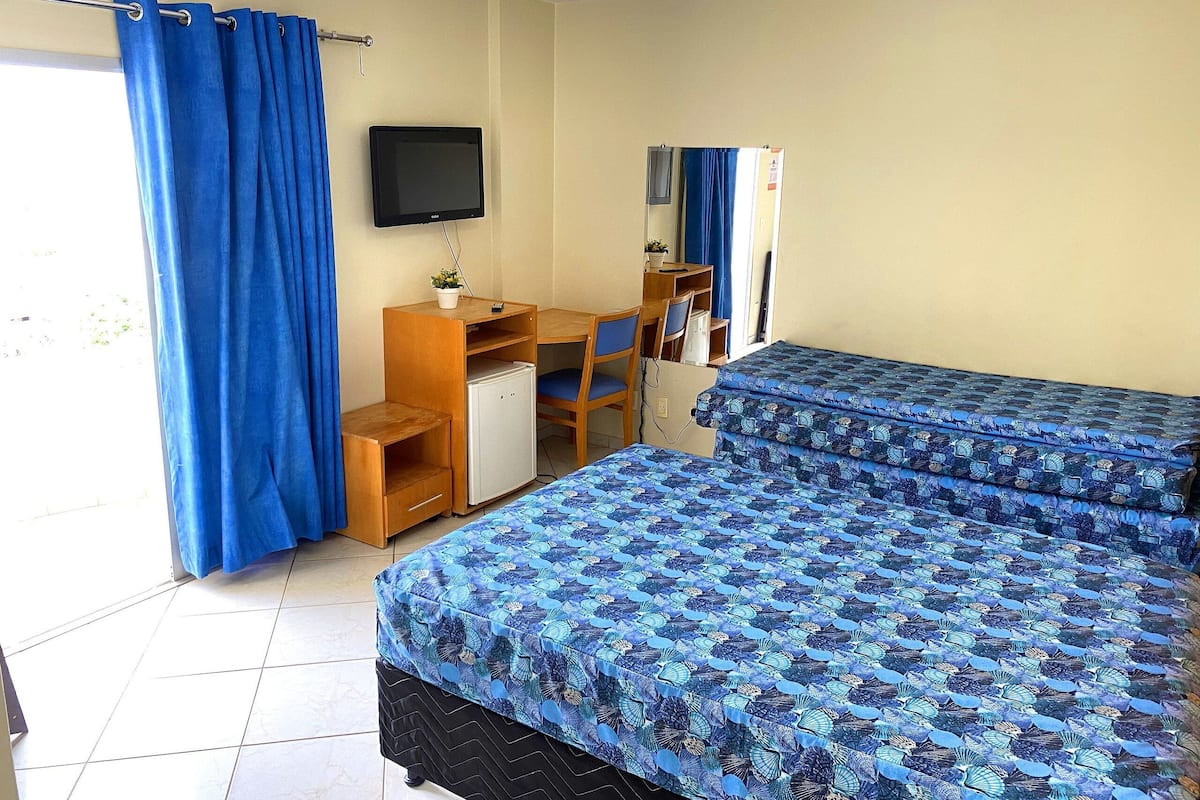 A room with a bed, a desk, a chair, a television, and a window with curtains.