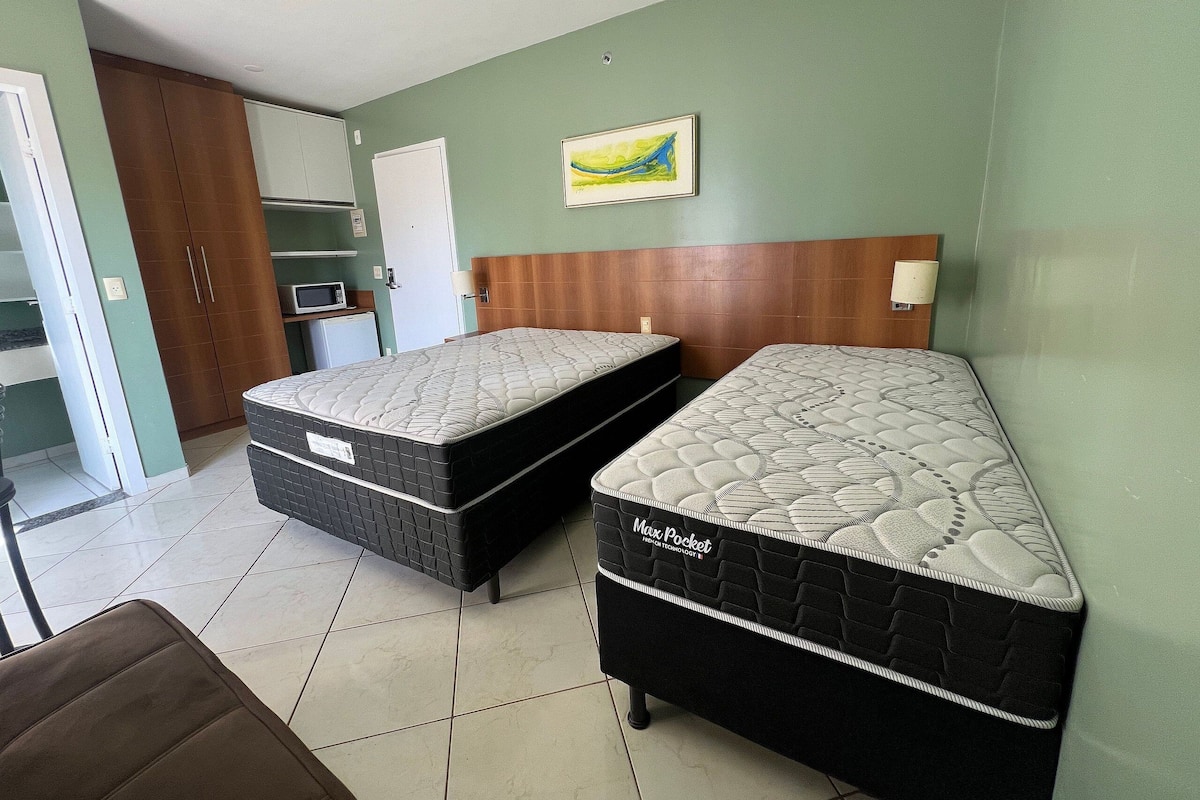 A room with two beds, a wooden headboard, a painting, and a microwave.