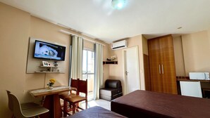 Quarto de hotel com cama, escrivaninha com cadeira, televisão e ar condicionado.