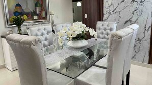Un comedor con una mesa de vidrio, sillas blancas tapizadas y un jarrón con flores blancas.
