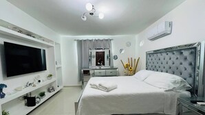 Un dormitorio moderno con una cama grande, un televisor, un tocador con espejo y una lámpara en el techo.