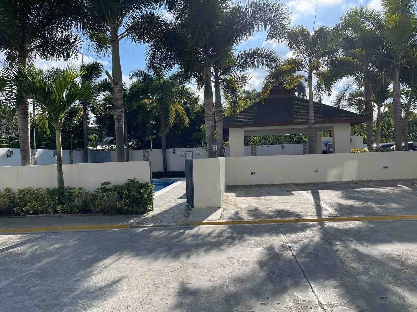 A gated parking area with palm trees and a small pavilion.