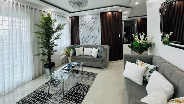 Una sala de estar moderna con un sofá gris, una mesa de centro de vidrio y una planta grande en maceta.