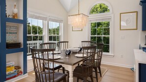 A dining area with a wooden table set for six, surrounded by chairs, with a chandelier above. - Walk to Beach, Heated Pool, Hot Tub, Dogs OK! (Kitty Hawk)